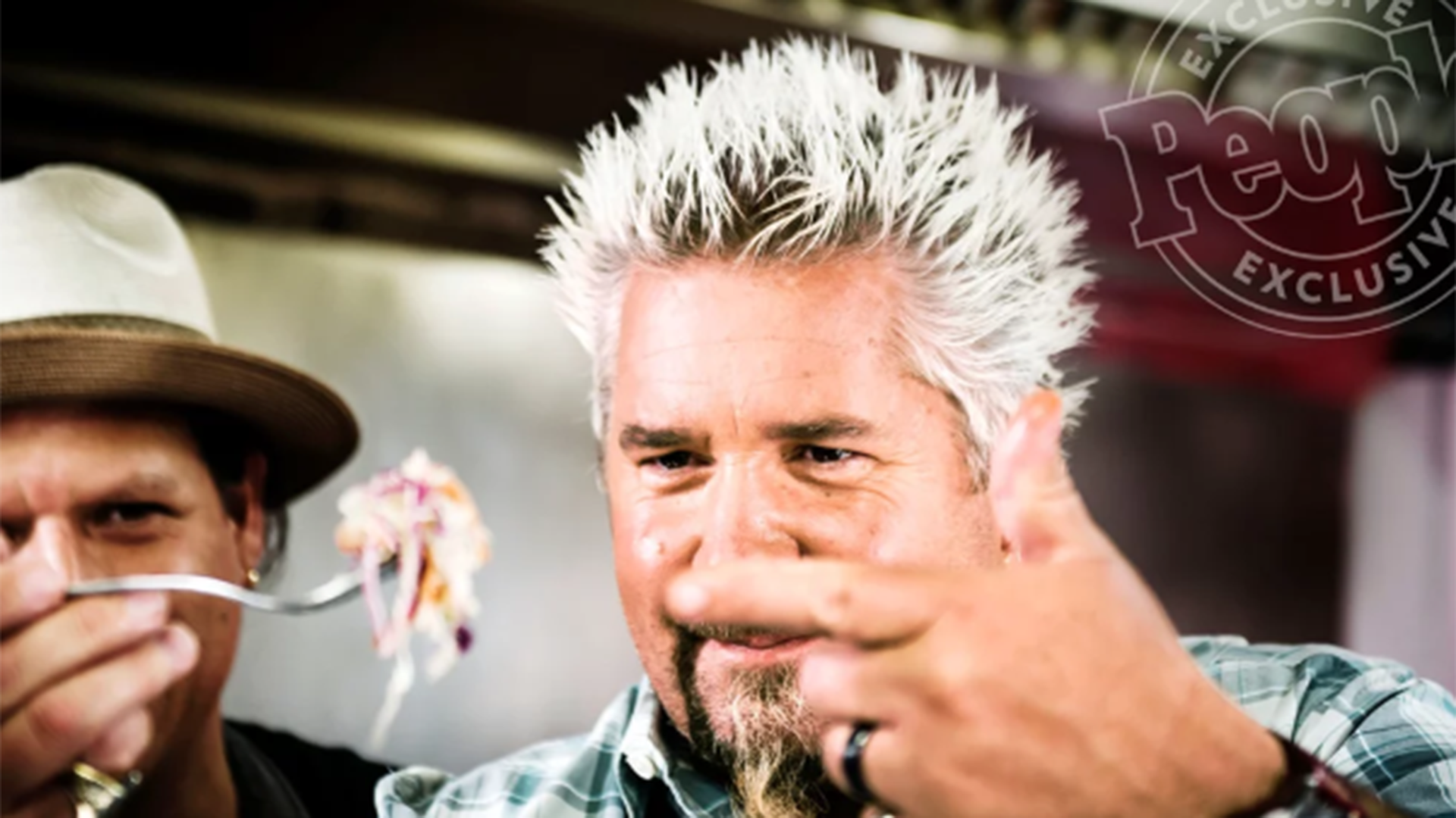 Guy Fieri, complete with signature haircut, prepares to taste a bite of pasta.