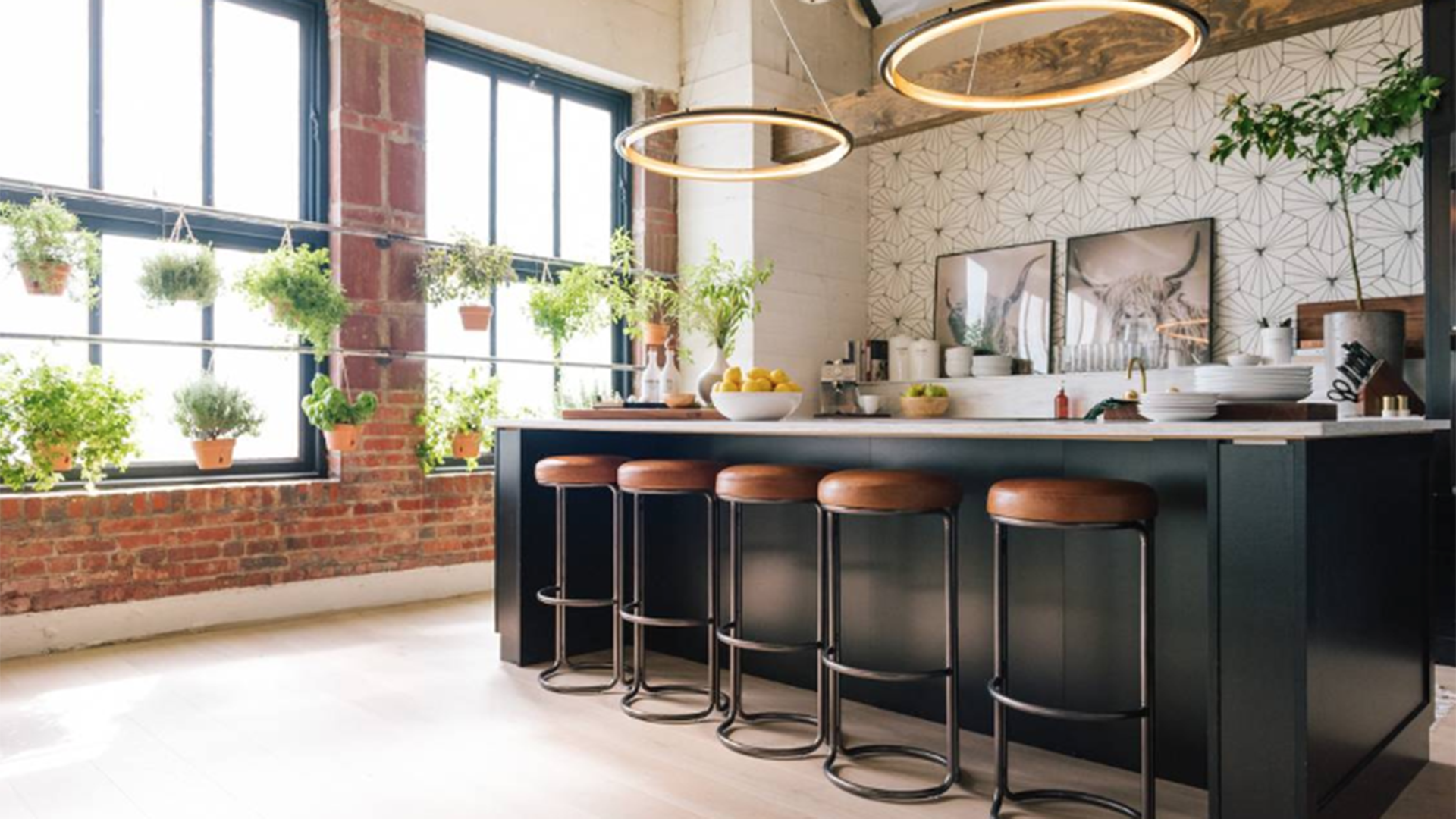 The loft residence of the cast of Netflix's Queer Eye makeover show features tall windows, natural light, and sleek decor including leather bar stools and circular lights above the kitchen counter. 